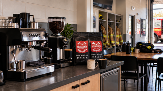 Two Fire Rescue Coffee Fire Station Roast bags beside an espresso machine in an Australian fire station kitchen